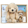 ROOM TO BLOOM That's My Puppy Baby Gift Hamper set arranged in a light wood box, featuring a beige plush puppy toy, a book, a growsuit, wrap and beanie set, and a teether.
