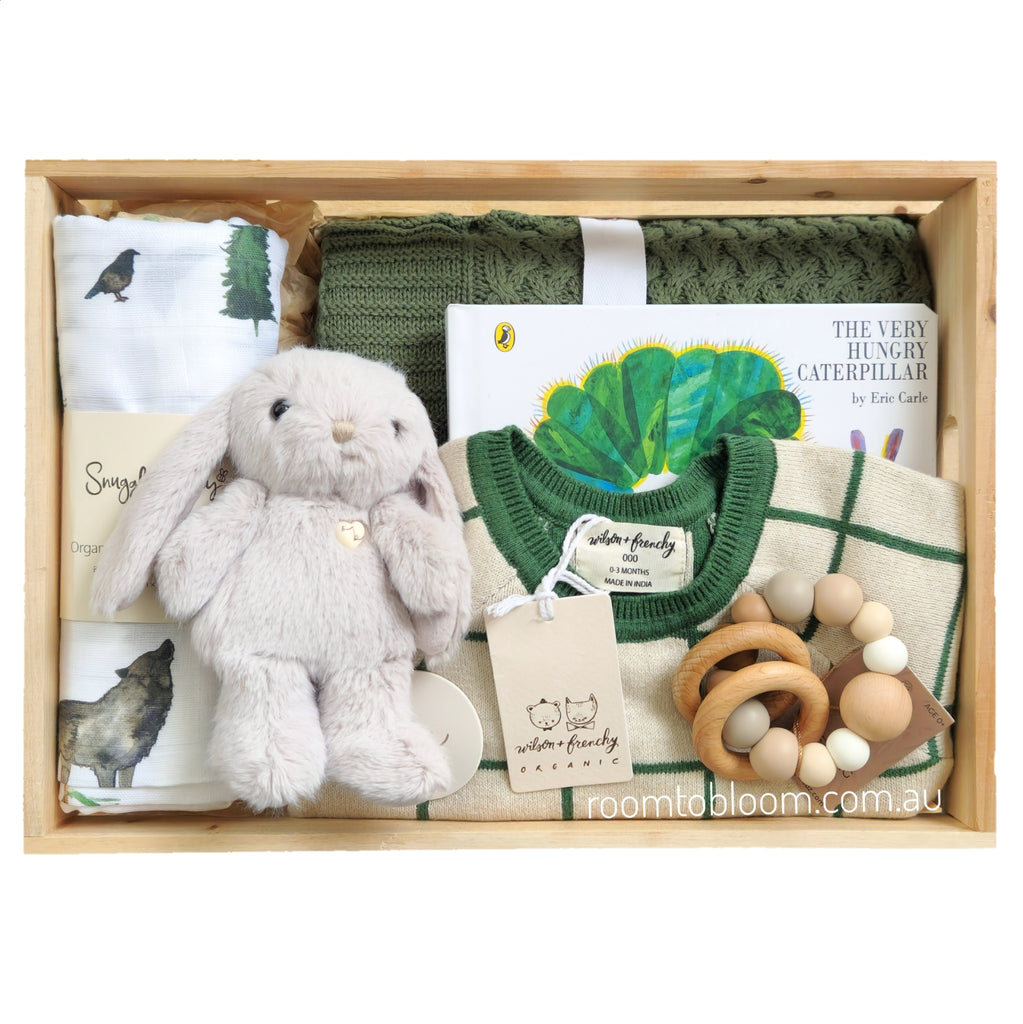 ROOM TO BLOOM Arcadia Baby Gift Hampert set arranged inside a light wood box, featuring a pale beige plush bunny, a green check knit baby growsuit, a book titled 'The Very Hungry Caterpillar', a small wooden teething toy, a green blanket, and muslin swaddle.