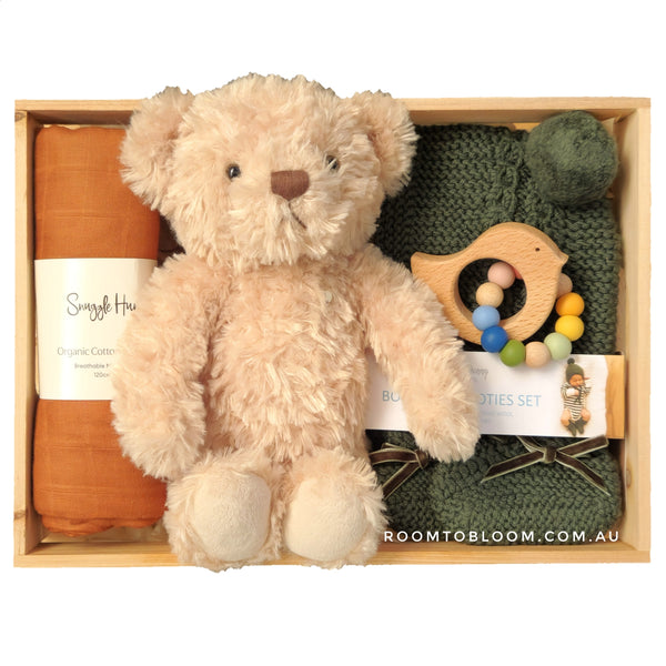 ROOM TO BLOOM Bear Essentials Baby Gift Hamper set with teddy bear, baby swaddle, teething ring, and other items in a wooden box.