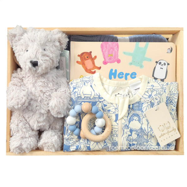 ROOM TO BLOOM Beary Tales Baby Gift Hamper set in a light wood box featuring a soft gray plush teddy bear, a blue and white patterned baby zips, a wooden beaded teether, and a colorful book