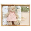 ROOM TO BLOOM Blessings Baby Gift Hamper set in a light wood box featuring a plush teddy bear wearing a pink dress, folded white swaddle with floral embroidery, a green bow, Lamington socks, and baby milestone cards.