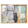 ROOM TO BLOOM Calm Palm Baby Gift Hamper set arranged in a light wood box, featuring a plush grey bunny toy, a mint green textured blanket, a folded white swaddle, a black hand cream tube, a wooden baby brush, a wooden teething ring with mint and white beads, and sage mittens. 