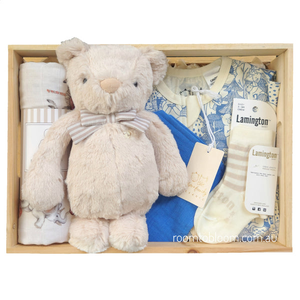 ROOM TO BLOOM Circus Fun Baby Gift Hamper set arranged in a light wood box, featuring a cream plush teddy bear with a striped bow tie, a zipsuit, and Lamington socks and a bib.