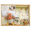 ROOM TO BLOOM Clucky Charm Baby Gift Hamper set arranged in a light wood box, including a Stretch Cotton Baby Wrap Set, a plush rooster toy, a wooden teething ring, and other baby items.