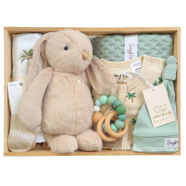 ROOM TO BLOOM Copacabana Baby Gift Hamper set in a light wood box featuring a plush beige bunny toy, a printed cotton romper and swaddle, a mint green knit blanket, a wooden ring teether with pastel beads, a beanie and socks.