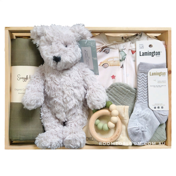 ROOM TO BLOOM Baby gift box with teddy bear, socks, and other items in a wooden box.