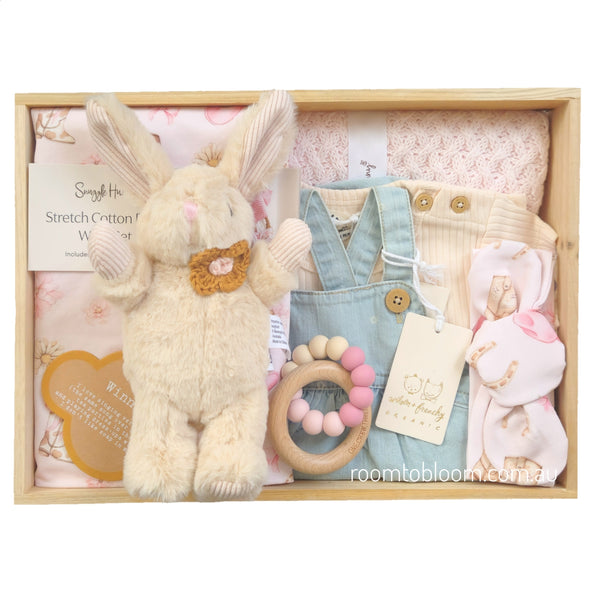ROOM TO BLOOM Daisy Doe Baby Gift Hamper set in a light wood box featuring a pink blanket, pink printed wrap and headband set, a plush cream bunny toy, a light blue denim overalls outfit, cream t-shirt, and a wooden bead teether.