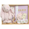 ROOM TO BLOOM Delightfully Dainty Baby Gift Hamper set arranged in a light wood tray, featuring a soft pink plush bunny, a lilac baby book with gold 'BABY' lettering, pale pink mittens, a floral jersey wrap and headband, and a wooden bead teether.