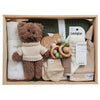 ROOM TO BLOOM The Woods Baby Gift Hamper set arranged in a light wood box, featuring a brown plush teddy bear in a cream knit sweater, a white swadle with gold stars, a green knit baby blanket, wooden bead teething ring, mittens, beanie and Lamington socks.