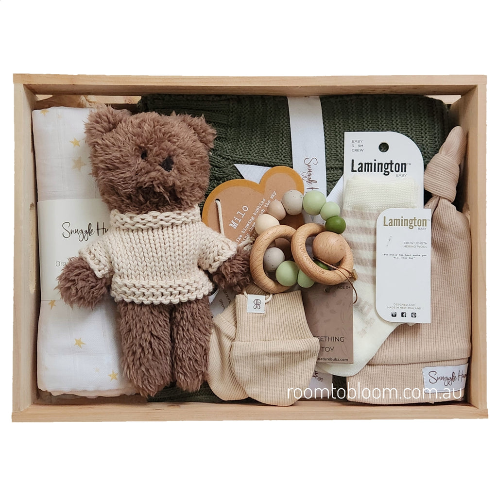 ROOM TO BLOOM The Woods Baby Gift Hamper set arranged in a light wood box, featuring a brown plush teddy bear in a cream knit sweater, a white swadle with gold stars, a green knit baby blanket, wooden bead teething ring, mittens, beanie and Lamington socks.