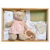 ROOM TO BLOOM Forever Friends Baby Gift Hamper set arranged inside a light wood box on a white background. The set includes a beige teddy bear wearing a pale pink dress, folded white baby clothes, a wooden bead teether, a green baby book with gold lettering, and a swaddle.
