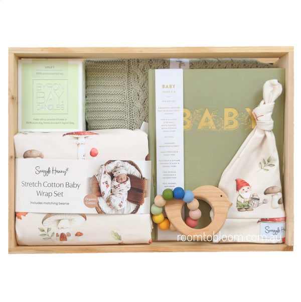 ROOM TO BLOOM Gnome Sweet Gnome Baby Gift Hamper set in a light wood box featuring a stretch cotton baby wrap set, a sage green baby book with gold lettering, a wooden teething ring with colorful beads, a candle and a knitted baby blanket.
