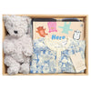 ROOM TO BLOOM Here, Bear & Everywhere Baby Gift Hamper set in a wooden box featuring a plush light grey teddy bear, a folded blue blanket,  a patterned baby romper, and a book.