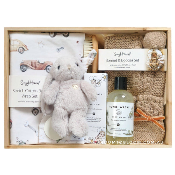 ROOM TO BLOOM  Joyful Journeys Baby Gift Hampert set with items including a plush toy, wrap, and bath products in a wooden box.