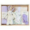 ROOM TO BLOOM Lovely Lilac Baby Gift Hamper set in a wooden box featuring a plush white bunny, a light purple cotton swaddle, a wooden bead teether with a lavender bead, a cream blanket, a floral baby romper, and a matching purple headband.