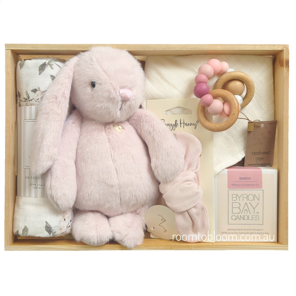 ROOM TO BLOOM Pink Posy Baby Gift Hamper set in a light wood box featuring a soft pink plush bunny, a folded floral swaddle, a wooden bead teething ring, a pink and white Enrich candle, a pink headband and a bandana bib.