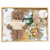 ROOM TO BLOOM Prairie Baby Gift Hamper set in a light wood box featuring a brown teddy bear wearing a cream knit sweater, a matching cotton wrap and beanie set, a green and white plaid baby growsuit, wooden and bead teething toy, and soft knit booties and blanket. 