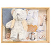 ROOM TO BLOOM Set Sail Baby Gift Hamper gift set in a light wood box featuring a fluffy grey plush teddy bear with cream jacket, a blue fabric bib, printed swaddle and beanie with nautical sailboat designs, pacifiers, and a book.
