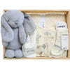 ROOM TO BLOOM Silver Wishes Baby Gift Hamper set in a wooden box featuring a large grey plush bunny, a cream baby bodysuit with illustrations, cream socks, a cream folded blanket, and a hairbrush.