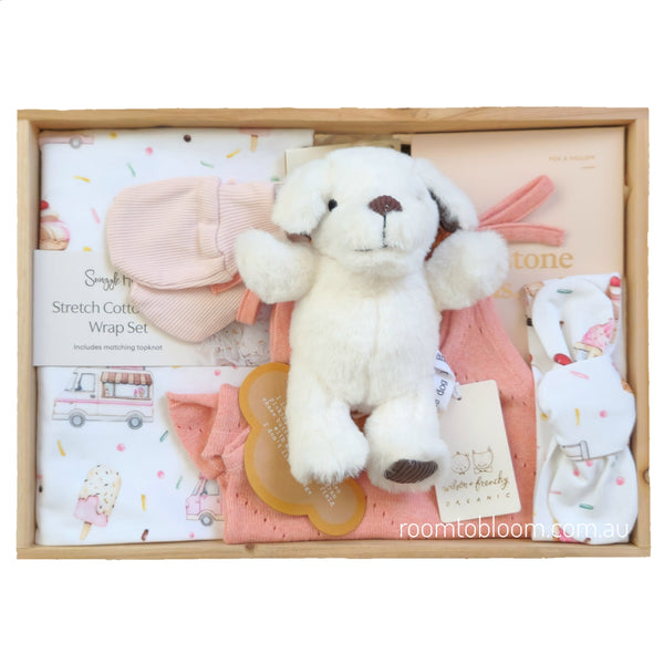 ROOM TO BLOOM Summer Lovin' Baby Gift Hamper set in a light wood box featuring a plush white puppy toy, a pink mittens, a white and pink stretch cotton wrap set, a peach baby outfit, and milestone cards.
