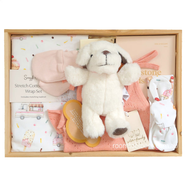 ROOM TO BLOOM Summer Lovin' Baby Gift Hamper set in a light wood box featuring a plush white puppy toy, a pink mittens, a white and pink stretch cotton wrap set, a peach baby outfit, and milestone cards.