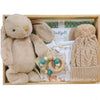 ROOM TO BLOOM Woodland Friends Baby Gift Hamper set arranged in a wooden box, featuring a plush beige bunny toy, a cream knit pom-pom hat, a wooden bead pacifier, baby clothing, a sage green blanket an more.