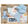 ROOM TO BLOOM Yee-Haw Baby Gift Hamper set arranged in a wooden box, featuring a plush brown bunny in light blue overalls, a light blue knit booties with pom-poms, a patterned baby swaddle and beanie, a bib and pacfiers.