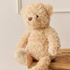 Beige SNUGGLE BUNNIES Arthur the Bear sitting on a wooden stool against a light background