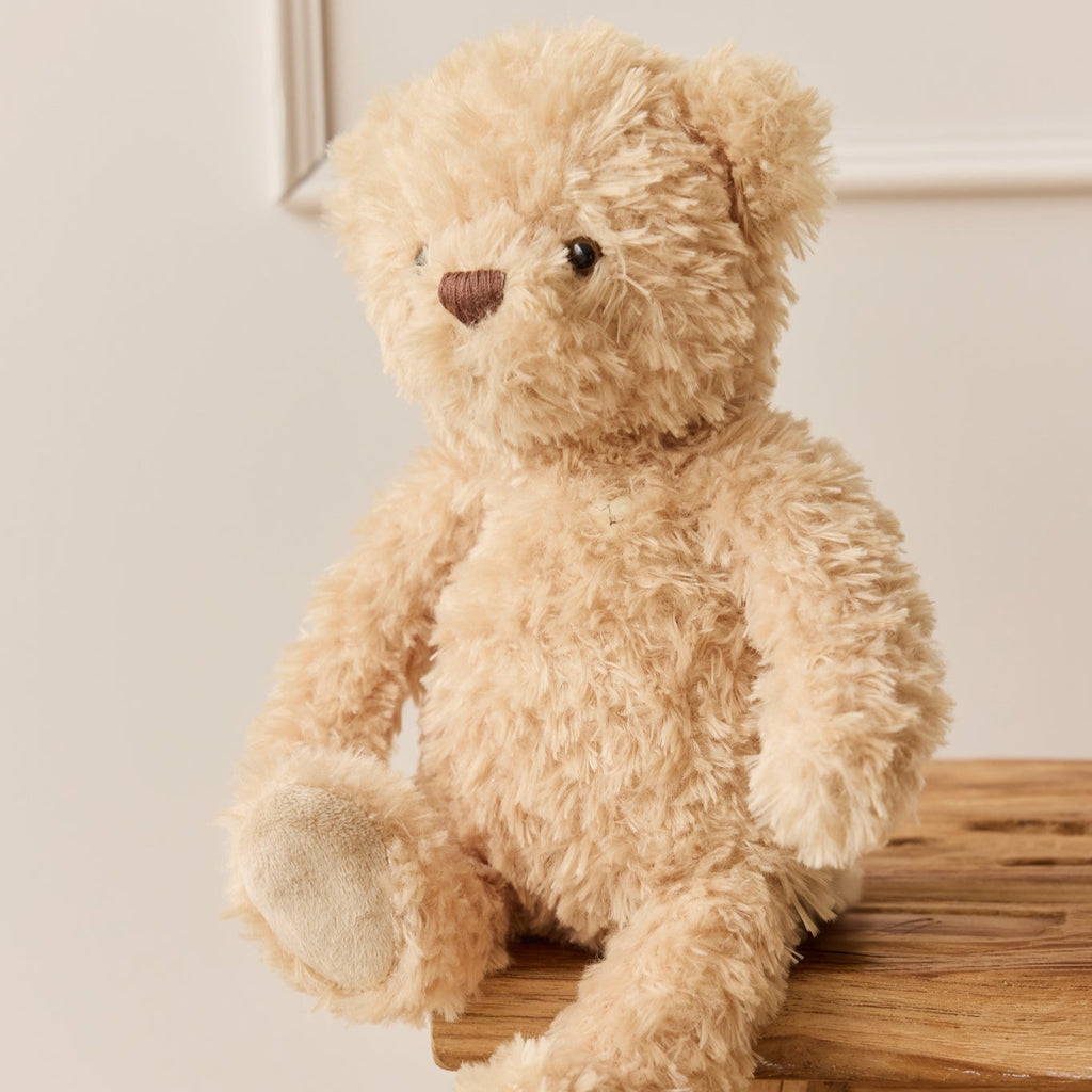 Beige SNUGGLE BUNNIES Arthur the Bear sitting on a wooden stool against a light background