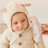 Baby in a cream-colored bunny suit holding a plush SNUGGLE BUNNIES Little Penelope - Beige toy with a neutral background