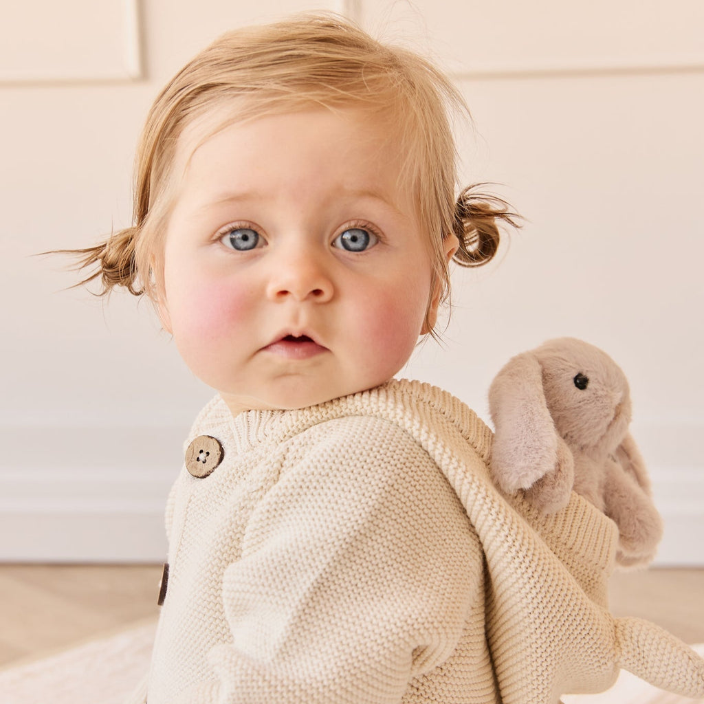 Baby wearing a beige knitted outfit sitting with a SNUGGLE BUNNIES Little Penelope - Beige.