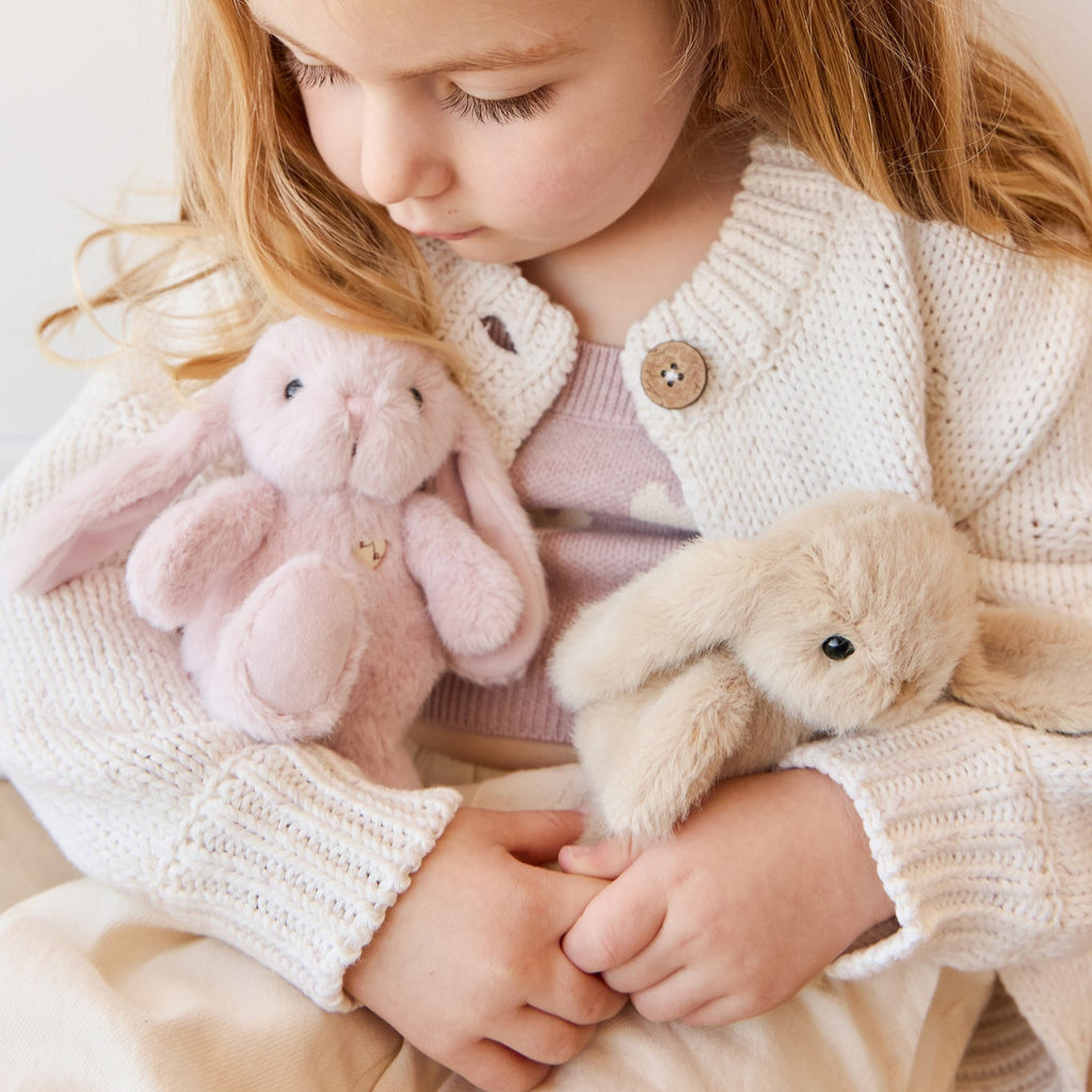 Child holding two plush toys, one SNUGGLE BUNNIES Little Penelope - Blossom and one beige, against a light background