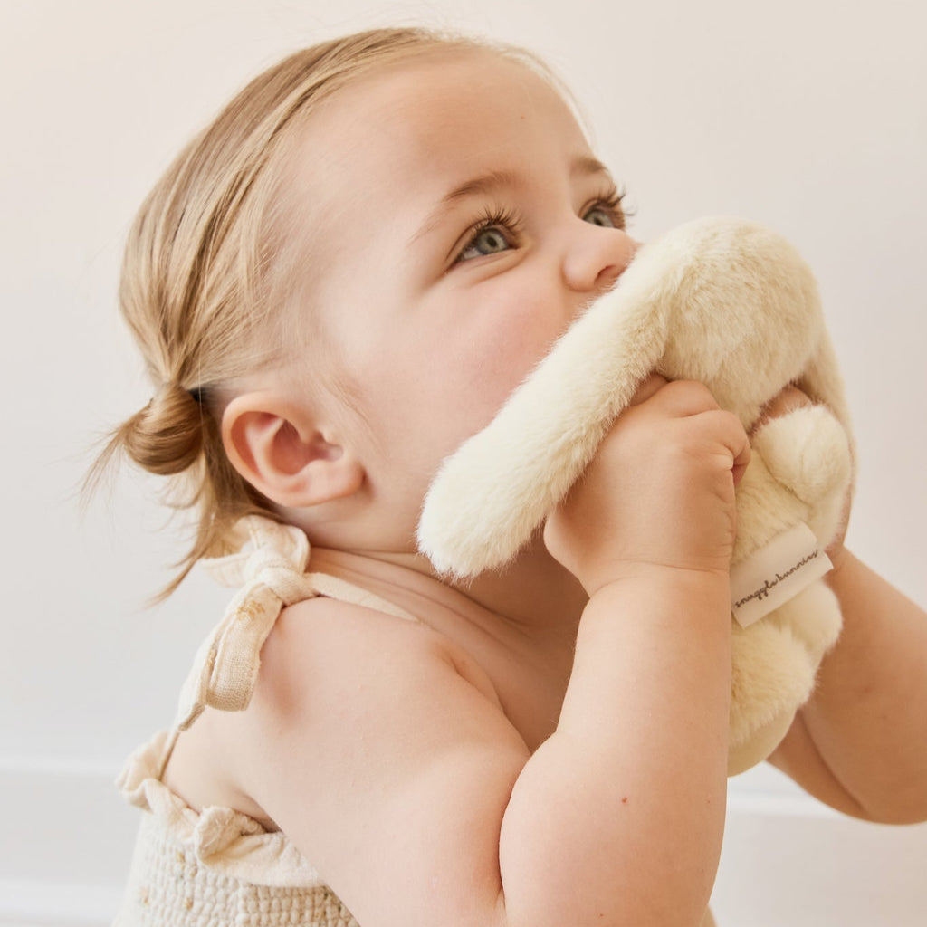 Baby holding a SNUGGLE BUNNIES Little Penelope - Sunshine toy in a softly lit room
