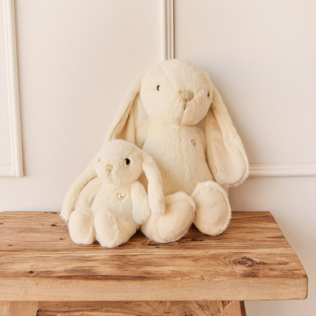 Two cream-colored SNUGGLE BUNNIES sitting on a wooden stool against a light wall.