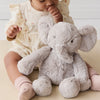 Baby sitting with a plush SNUGGLE BUNNIES Olive the Elephant toy wearing a white headband.
