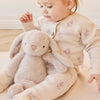 Child in a floral cardigan holding a plush SNUGGLE BUNNIES Penelope - Beige toy on a light wooden floor.