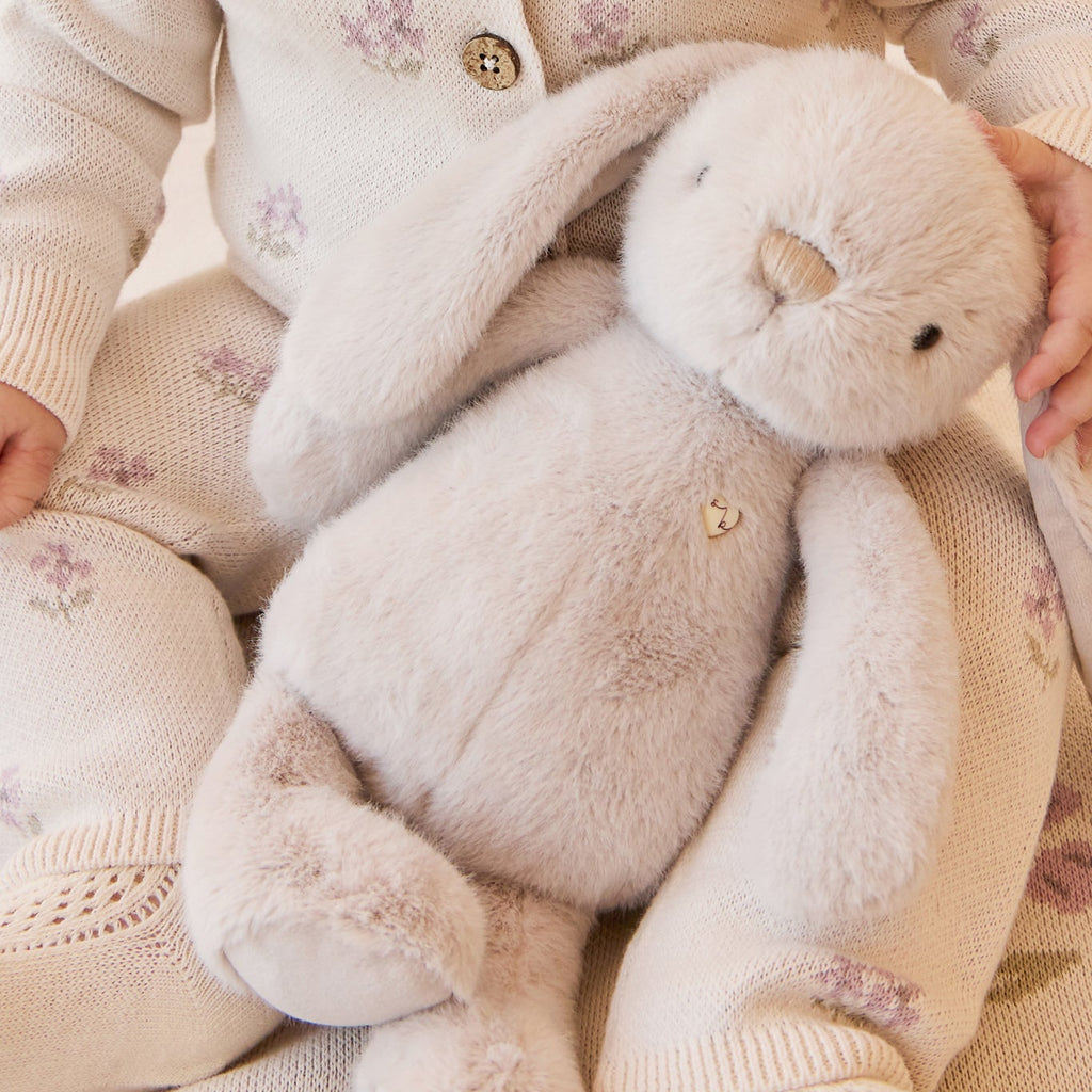 Child holding a SNUGGLE BUNNIES Penelope - Beige toy with floral patterns on clothing and background