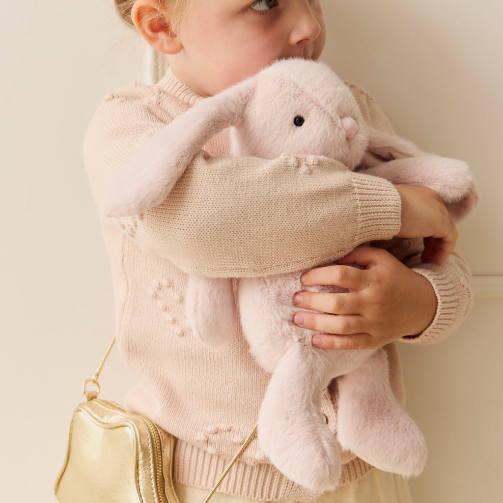 Young girl holding a pink plush SNUGGLE BUNNIES Penelope Bunny - Blossom toy against a plain background