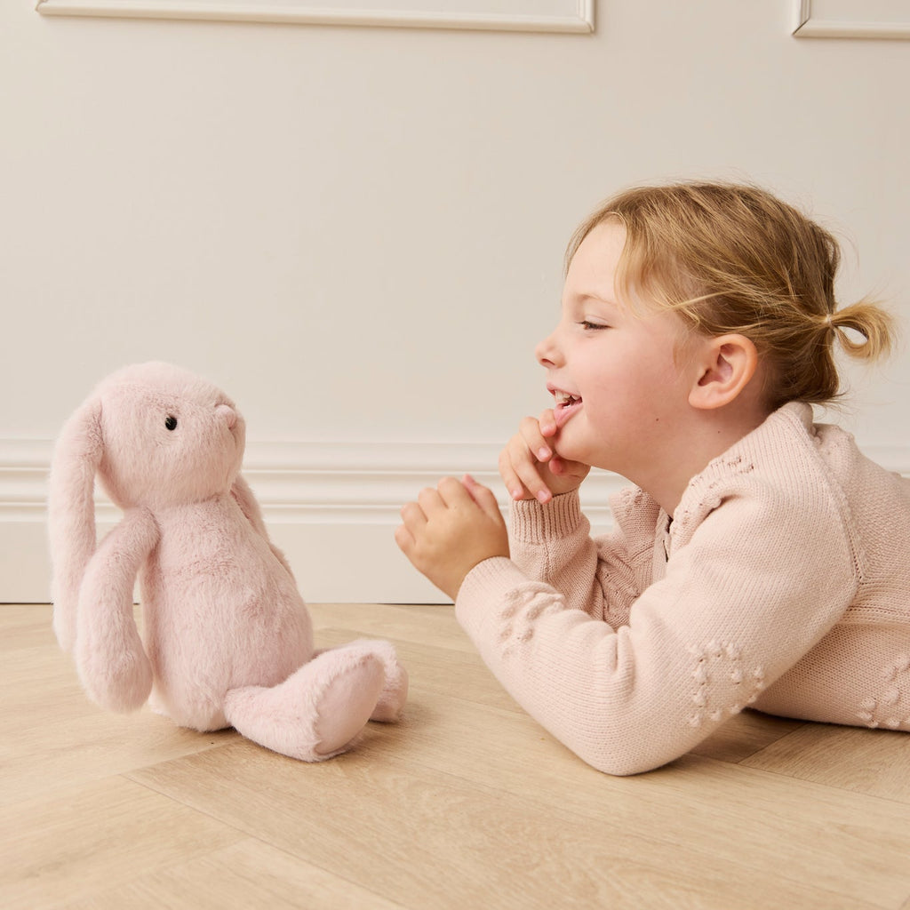Child playing with a plush SNUGGLE BUNNIES Penelope Bunny - Blossom toy on a wooden floor.
