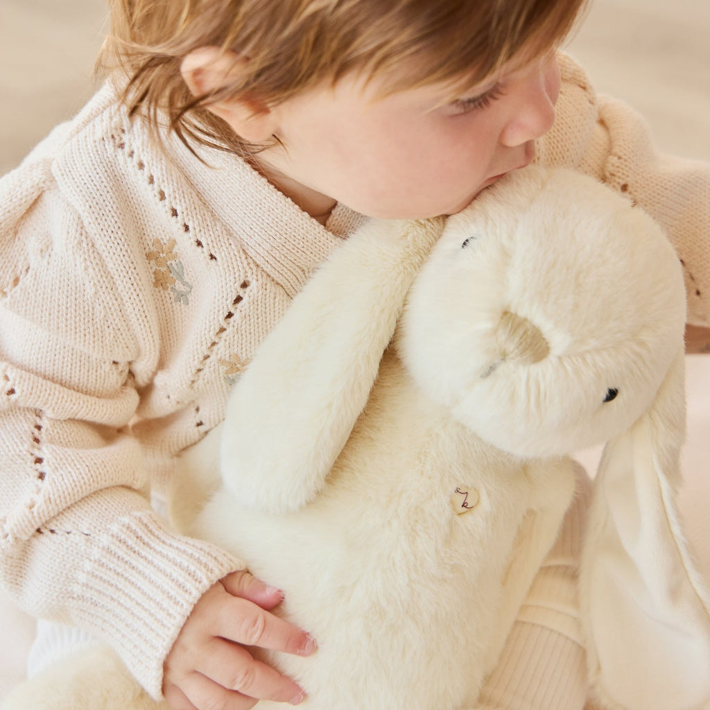 Child holding a plush SNUGGLE BUNNIES Penelope Bunny - Sunshine toy in a cozy setting