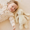 Baby lying next to a plush SNUGGLE BUNNIES Penelope Bunny - Sunshine toy on a soft surface