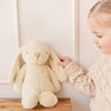 Child holding a plush SNUGGLE BUNNIES Penelope Bunny - Sunshine toy on a wooden stool against a white wall