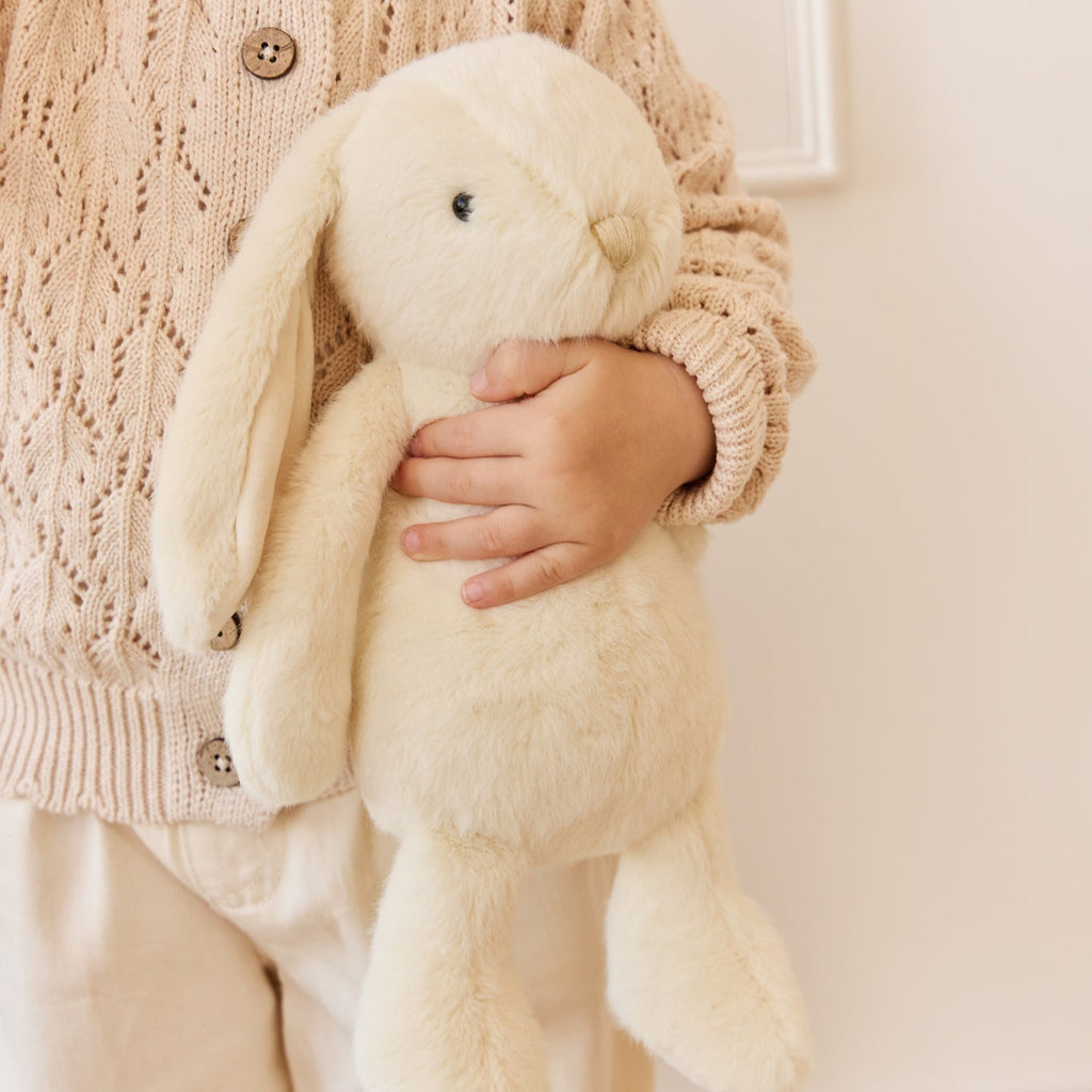 Child holding a plush SNUGGLE BUNNIES Penelope Bunny - Sunshine toy wearing a knitted sweater.
