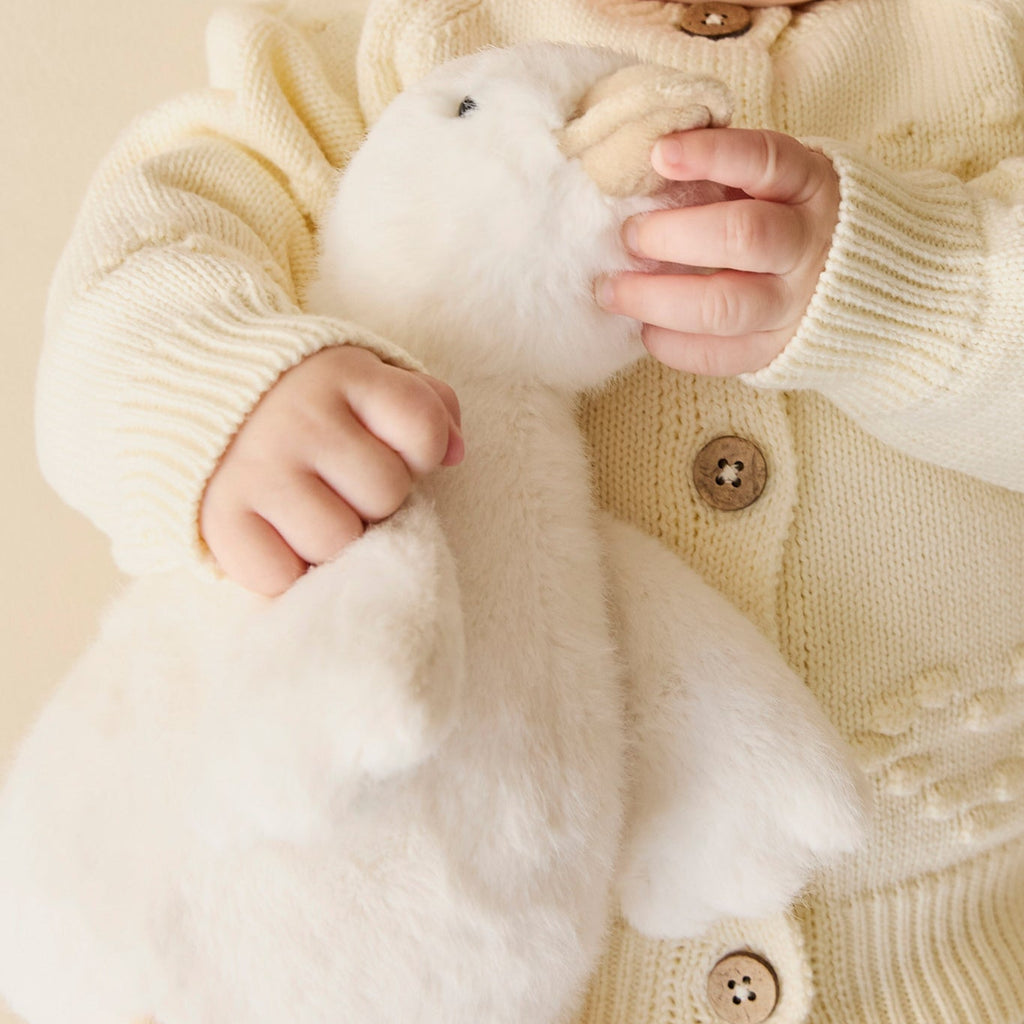 Baby holding a white plush SNUGGLE BUNNIES Rose the Duck toy against a neutral background