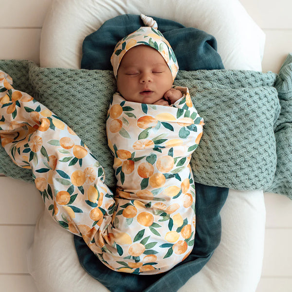 Newborn baby wrapped in a SNUGGLE HUNNY Organic Jersey Wrap & Beanie set - Sunny Citrus on a soft surface.