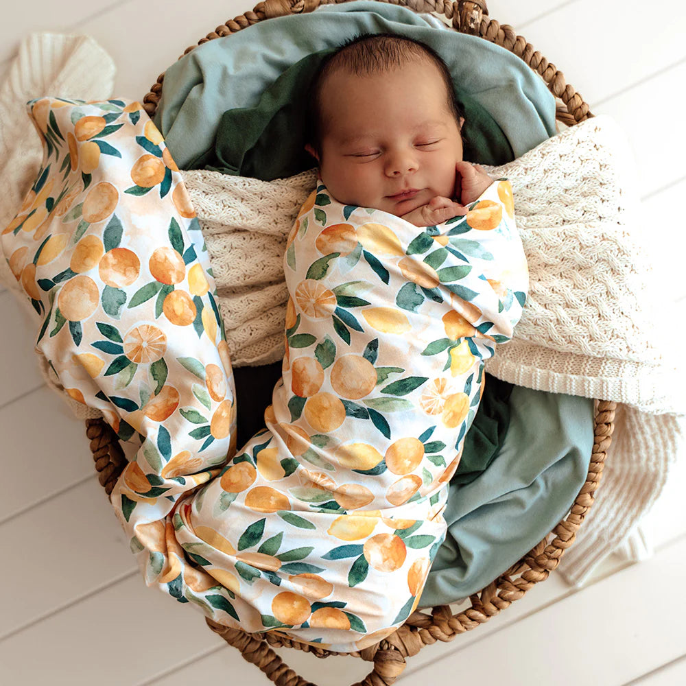 Newborn baby wrapped in a SNUGGLE HUNNY Organic Jersey Wrap & Beanie set - Sunny Citrus on a soft surface.