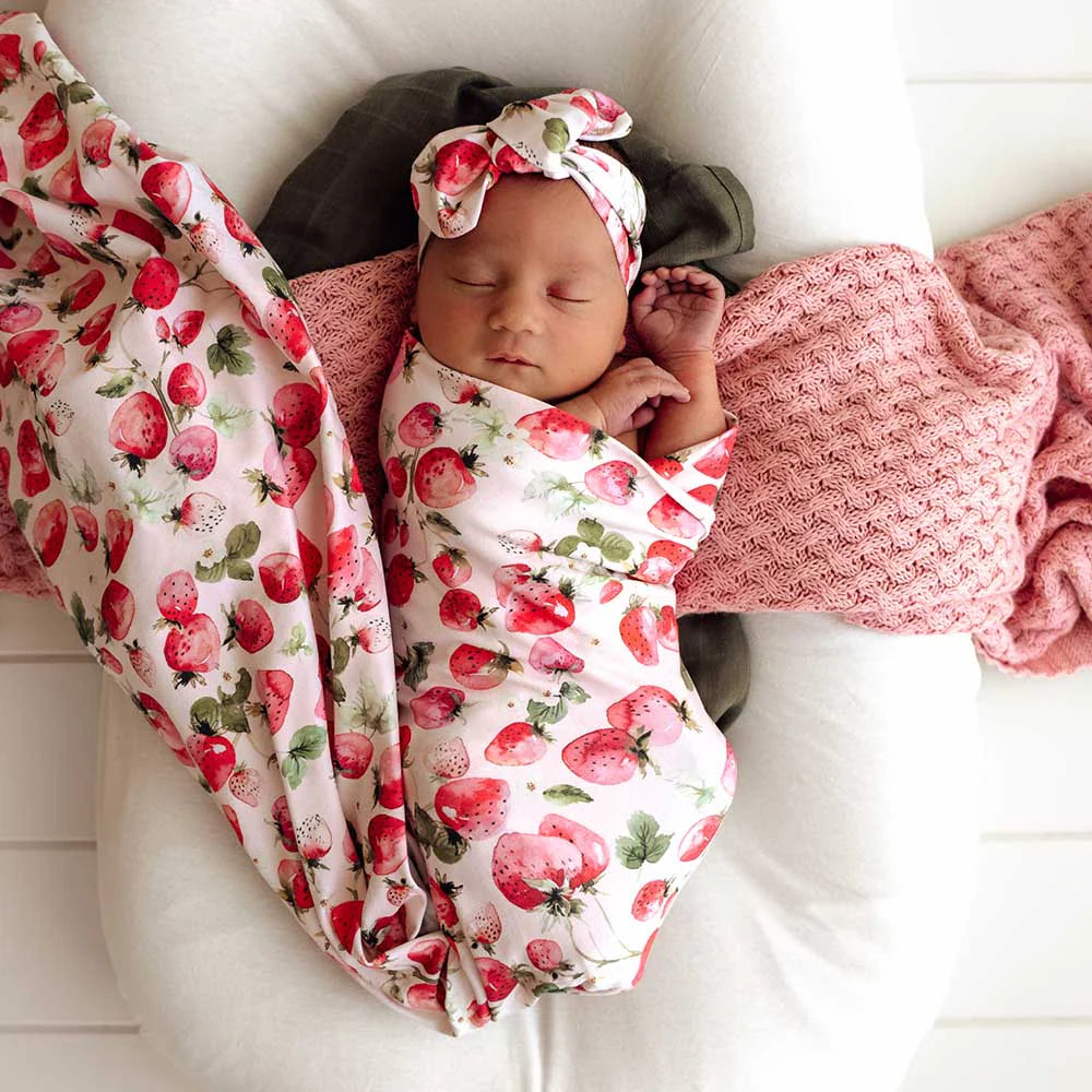 SNUGGLE HUNNY Jersey Wrap & Strawberry-patterned Topknot Set  swaddle with a matching headband, lying on a white surface.