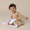 Baby wrapped in a SNUGGLE HUNNY Organic Hooded Baby Towel - Sunny Citrus on a beige background