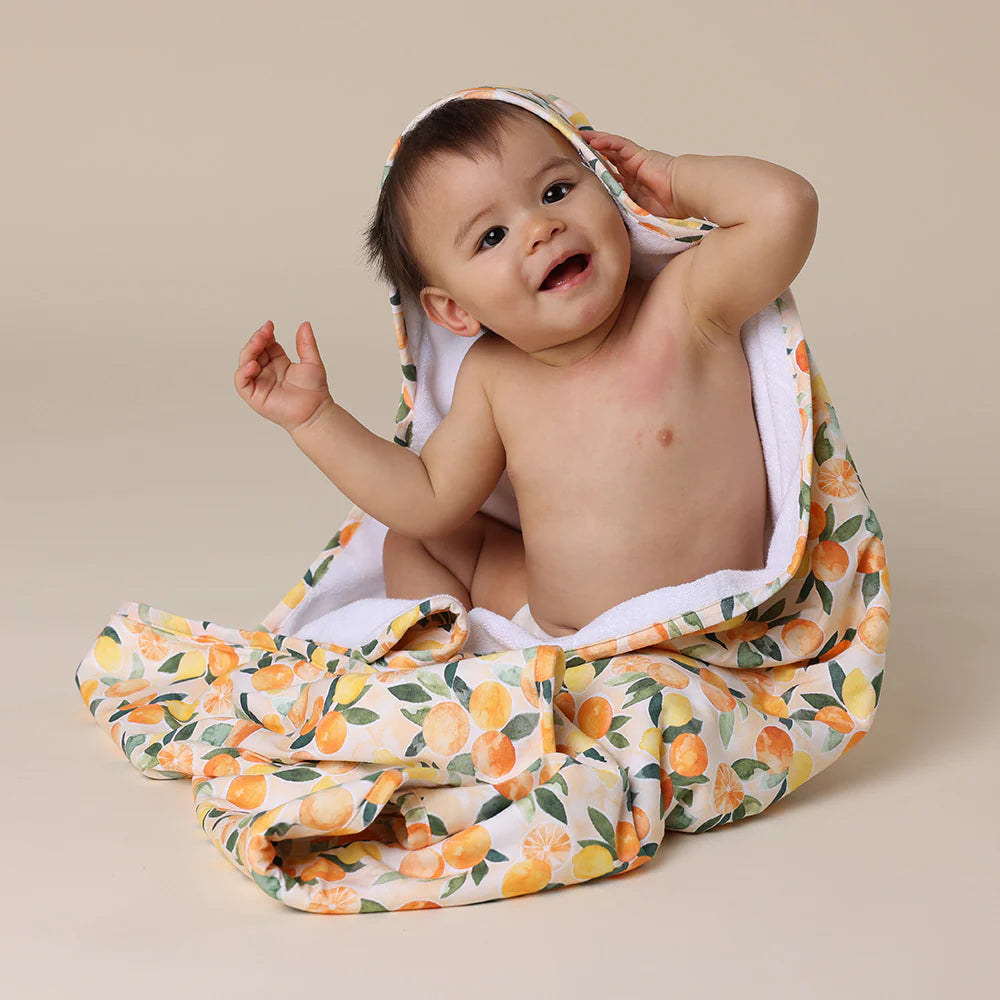 Baby wrapped in a SNUGGLE HUNNY Organic Hooded Baby Towel - Sunny Citrus on a beige background