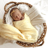 Newborn baby wrapped in a SNUGGLE HUNNY Organic Muslin Swaddle -  Sunlight with floral headband in a woven basket on a white background